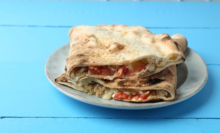 Photo of Halves of tasty calzone with meat, cheese and tomato on light blue wooden table, closeup