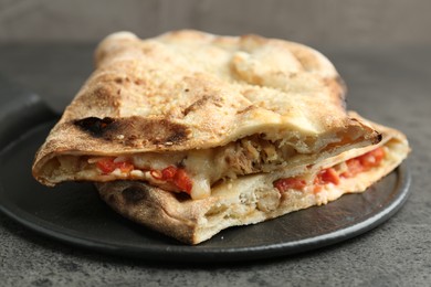 Photo of Halves of tasty calzone with meat, cheese and tomato on grey textured table, closeup