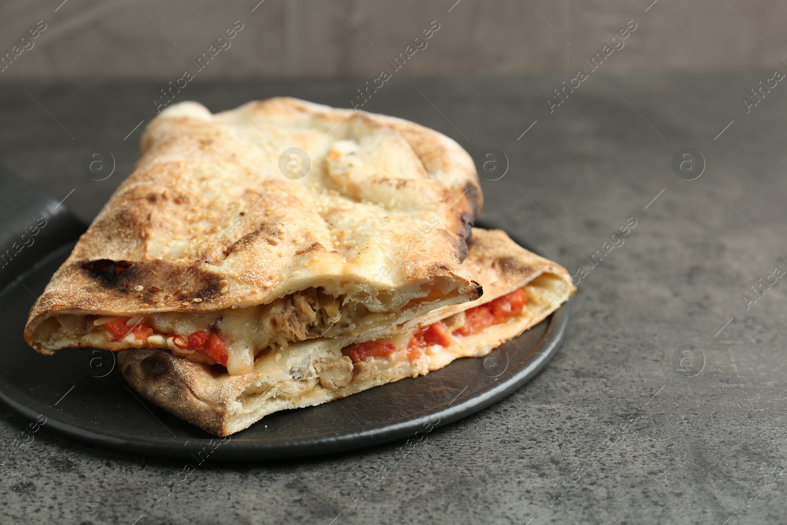 Photo of Halves of tasty calzone with meat, cheese and tomato on grey textured table, closeup. Space for text