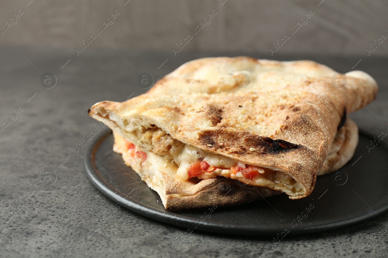 Photo of Halves of tasty calzone with meat, cheese and tomato on grey textured table, closeup. Space for text