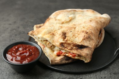 Halves of tasty calzone with meat, cheese, tomato and sauce on grey textured table, closeup