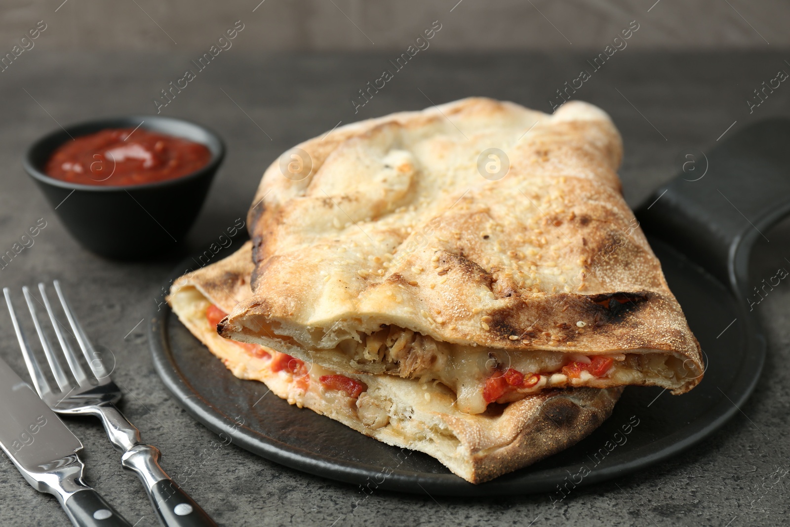 Photo of Halves of tasty calzone with meat, cheese, tomato and sauce on grey textured table, closeup