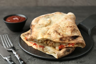 Halves of tasty calzone with meat, cheese, tomato and sauce on grey textured table, closeup