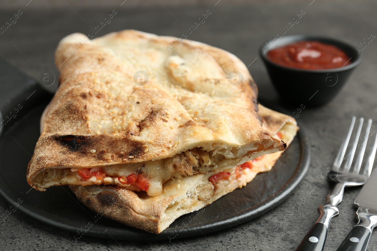 Photo of Halves of tasty calzone with meat, cheese, tomato and sauce on grey textured table, closeup