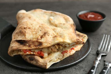 Photo of Halves of tasty calzone with meat, cheese, tomato and sauce on grey textured table, closeup