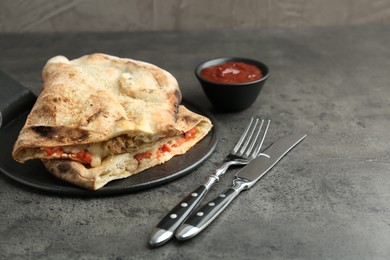 Halves of tasty calzone with meat, cheese, tomato and sauce on grey textured table. Space for text