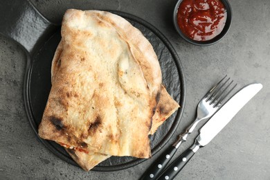 Halves of tasty calzone served with sauce on grey textured table, flat lay