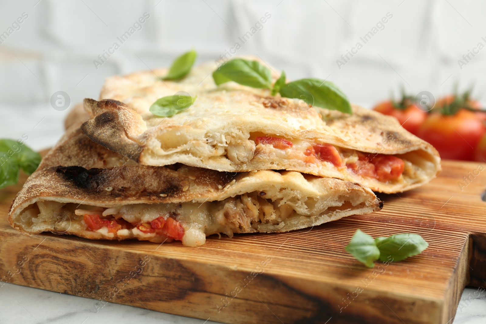 Photo of Halves of tasty calzone with meat, cheese, basil and tomato on white table, closeup