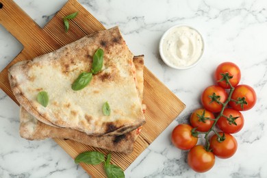 Halves of tasty calzone, basil, sauce and tomato on white marble table, flat lay