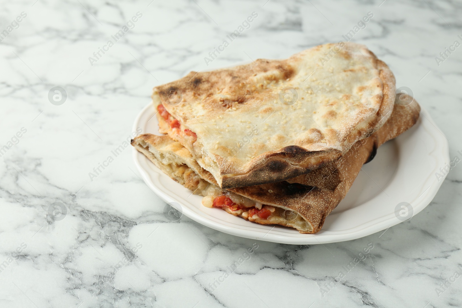 Photo of Halves of tasty calzone with meat, cheese and tomato on white marble table, closeup. Space for text