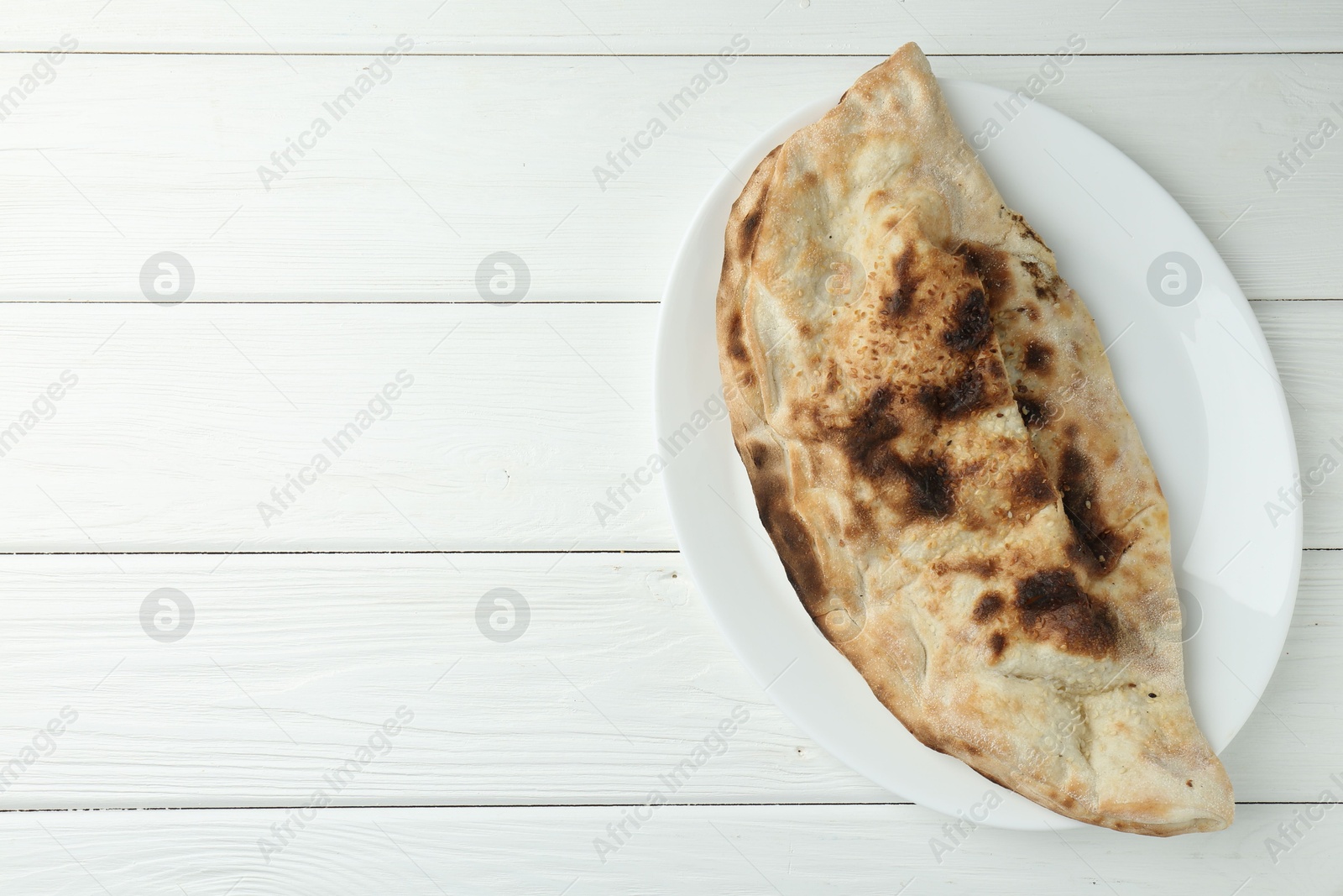 Photo of Plate with tasty calzone on white wooden table, top view. Space for text