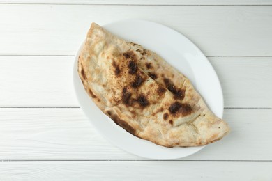 Photo of Plate with tasty calzone on white wooden table, top view