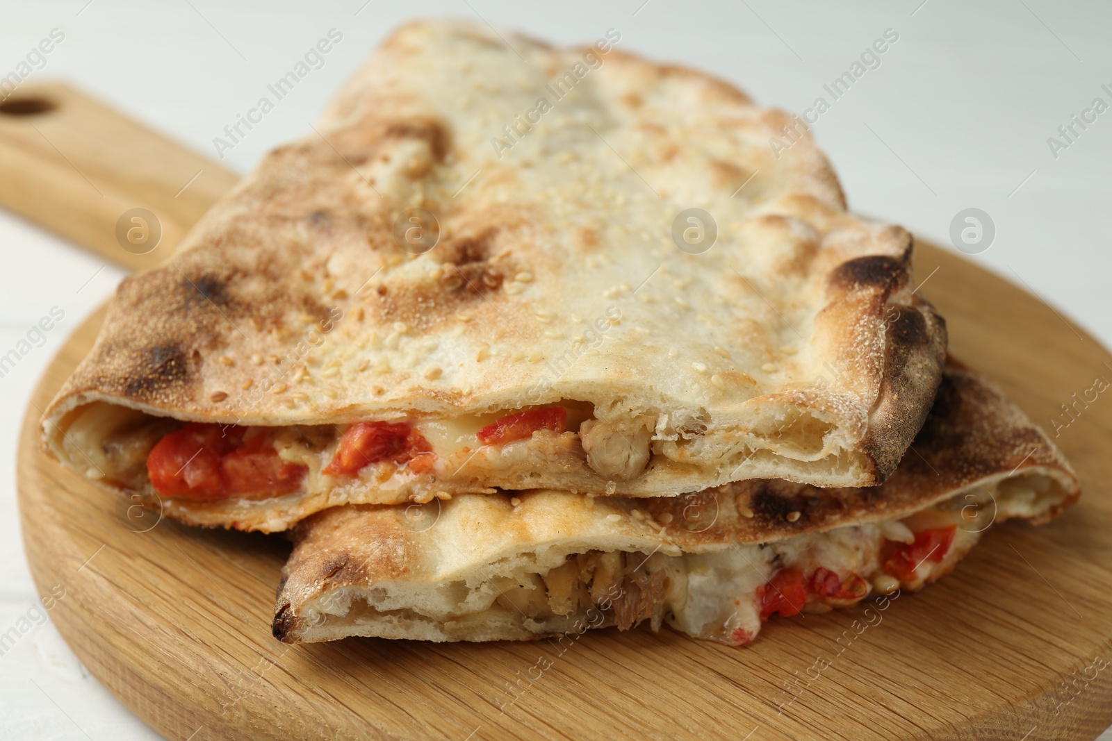 Photo of Halves of tasty calzone with meat, cheese and tomato on white wooden table, closeup