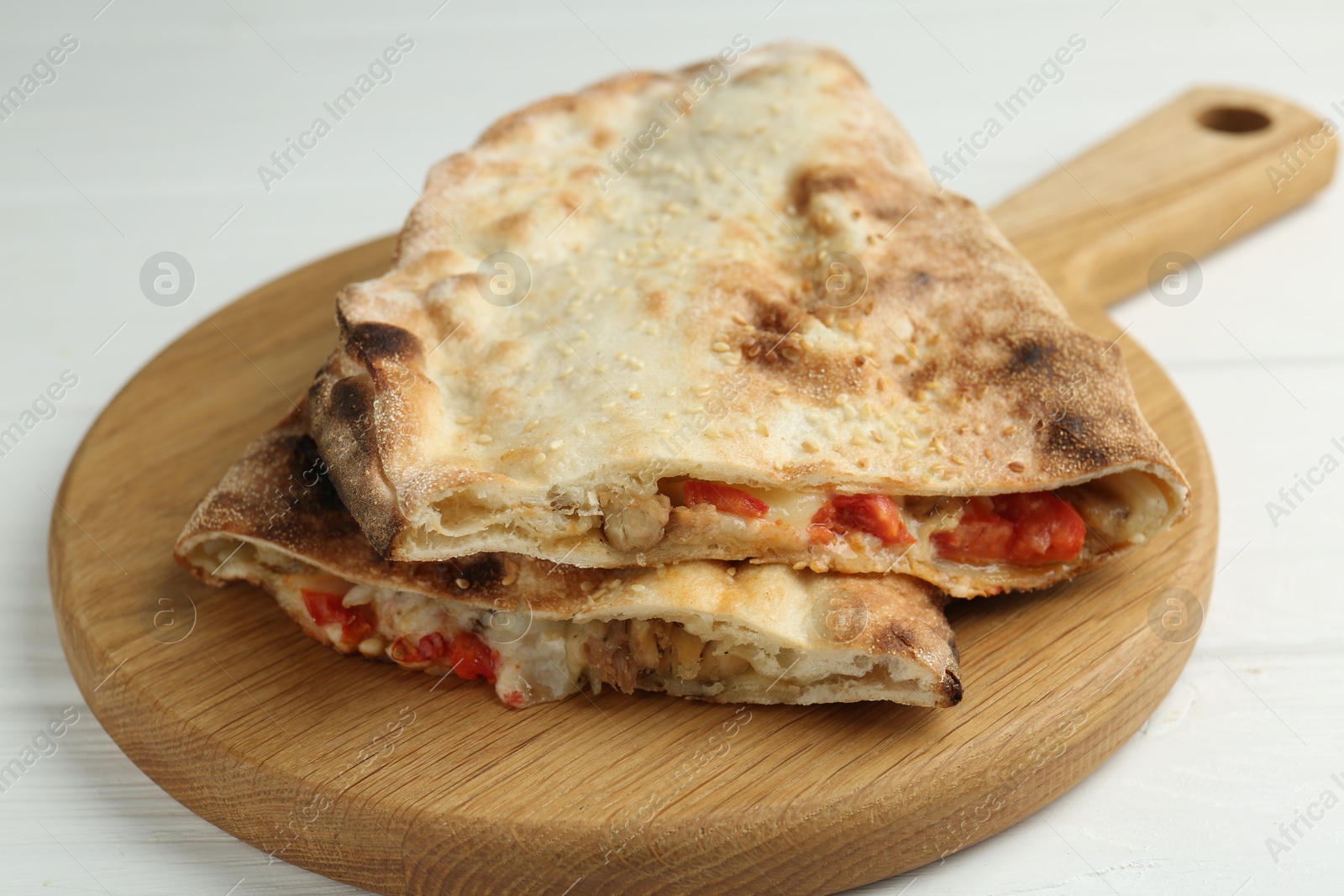 Photo of Halves of tasty calzone with meat, cheese and tomato on white wooden table, closeup