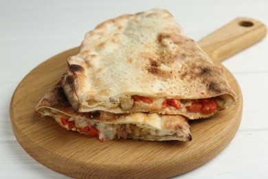 Halves of tasty calzone with meat, cheese and tomato on white wooden table, closeup