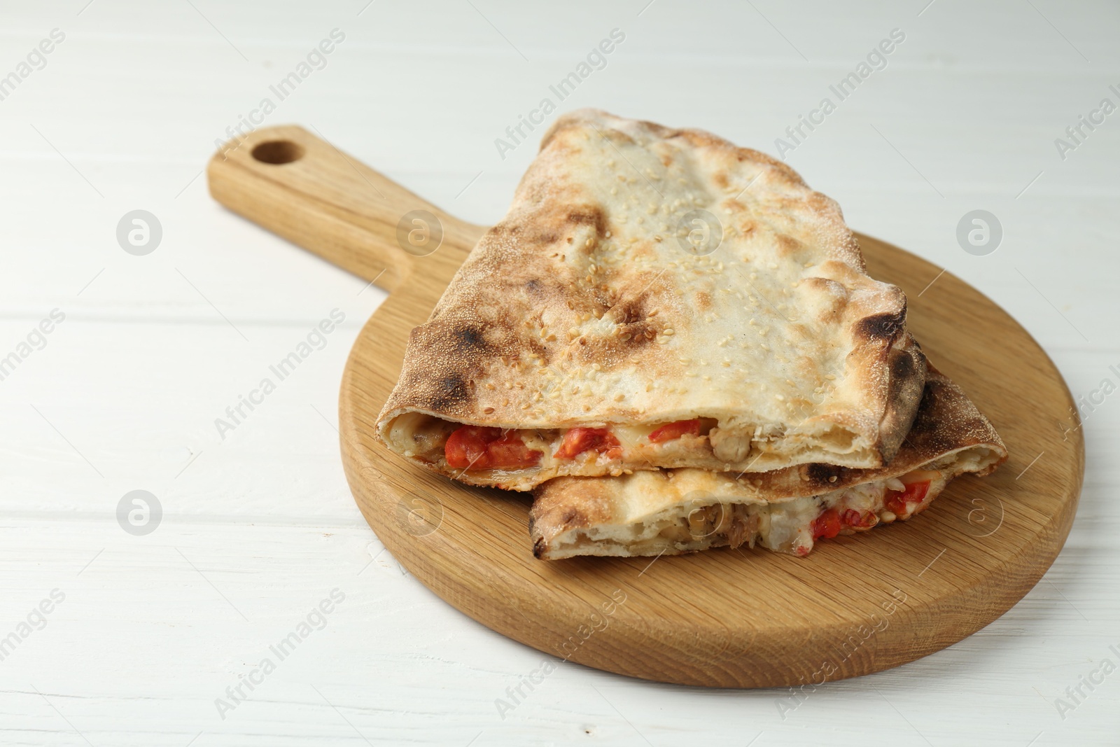 Photo of Halves of tasty calzone with meat, cheese and tomato on white wooden table, closeup