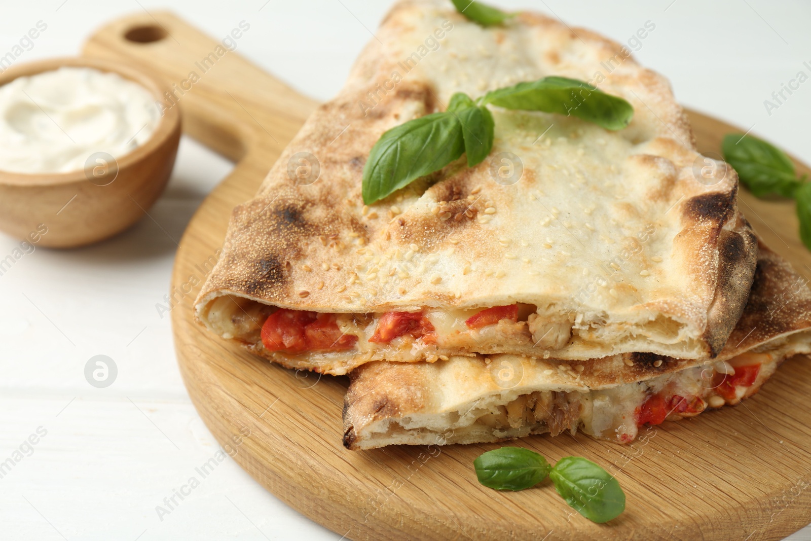 Photo of Halves of tasty calzone with meat, cheese, tomato, basil and sauce on white wooden table, closeup