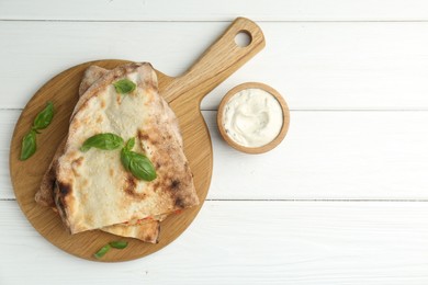 Halves of tasty calzone, basil and sauce on white wooden table, flat lay. Space for text