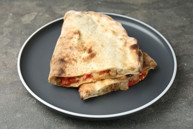 Halves of tasty calzone with meat, cheese and tomato on grey textured table, closeup