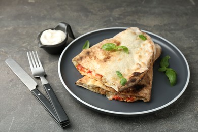 Halves of tasty calzone with meat, cheese, basil and tomato served with sauce on grey textured table, closeup