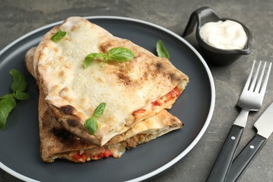 Halves of tasty calzone with meat, cheese, basil and tomato served with sauce on grey textured table, closeup