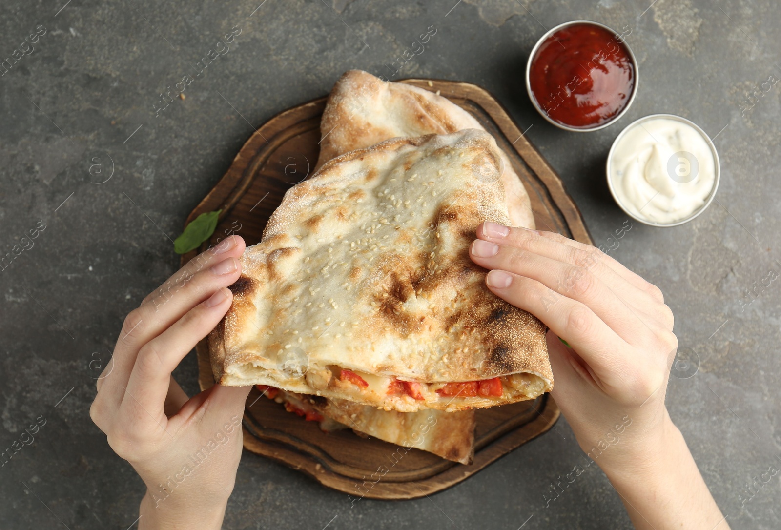 Photo of Woman eating tasty calzone with meat, cheese and tomato at grey textured table, top view