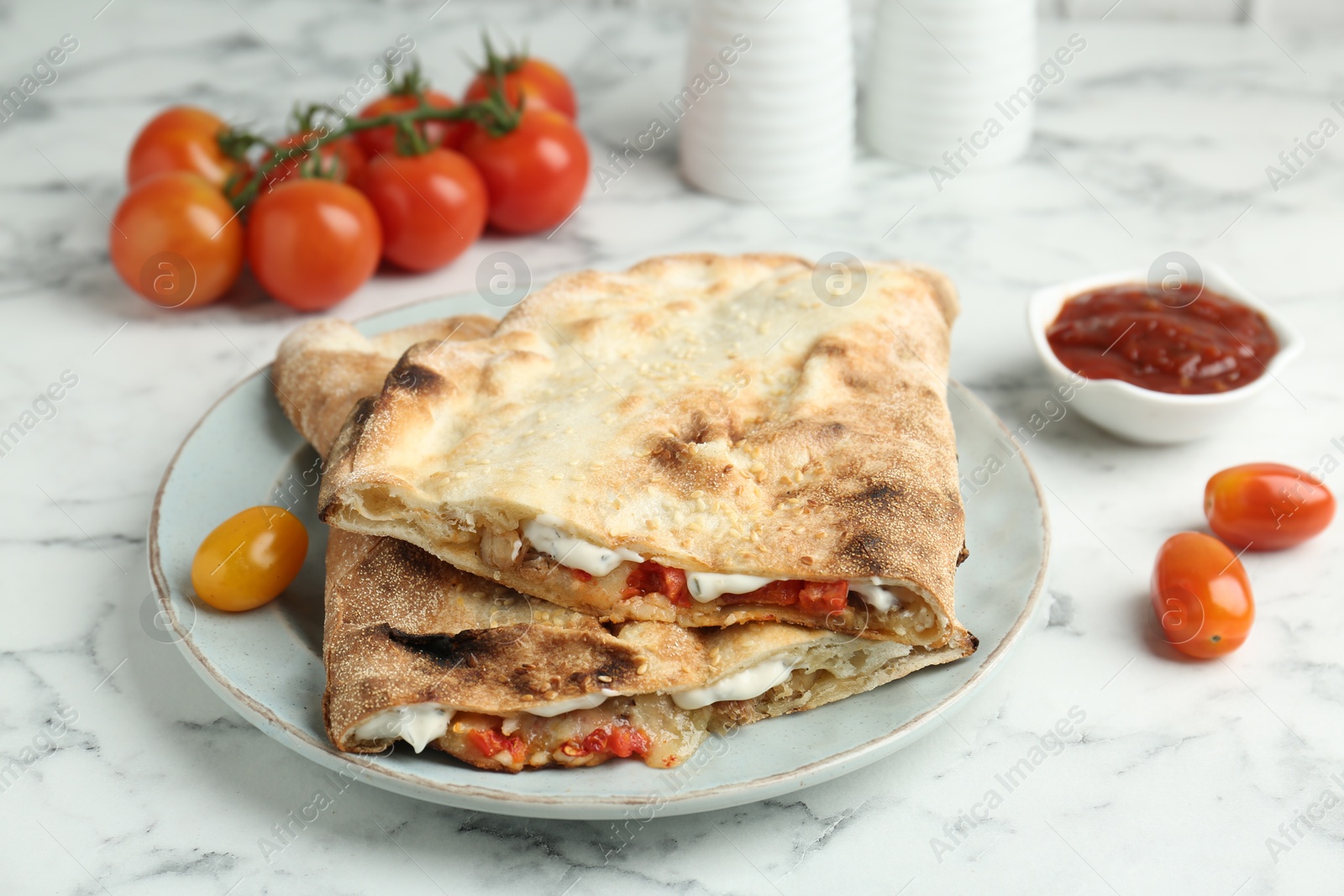 Photo of Halves of tasty calzone with meat, cheese, sauce and tomato on white marble table, closeup