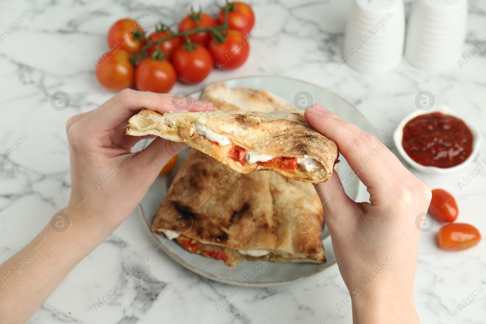 Photo of Woman eating tasty calzone with meat, cheese and tomato at white marble table, closeup