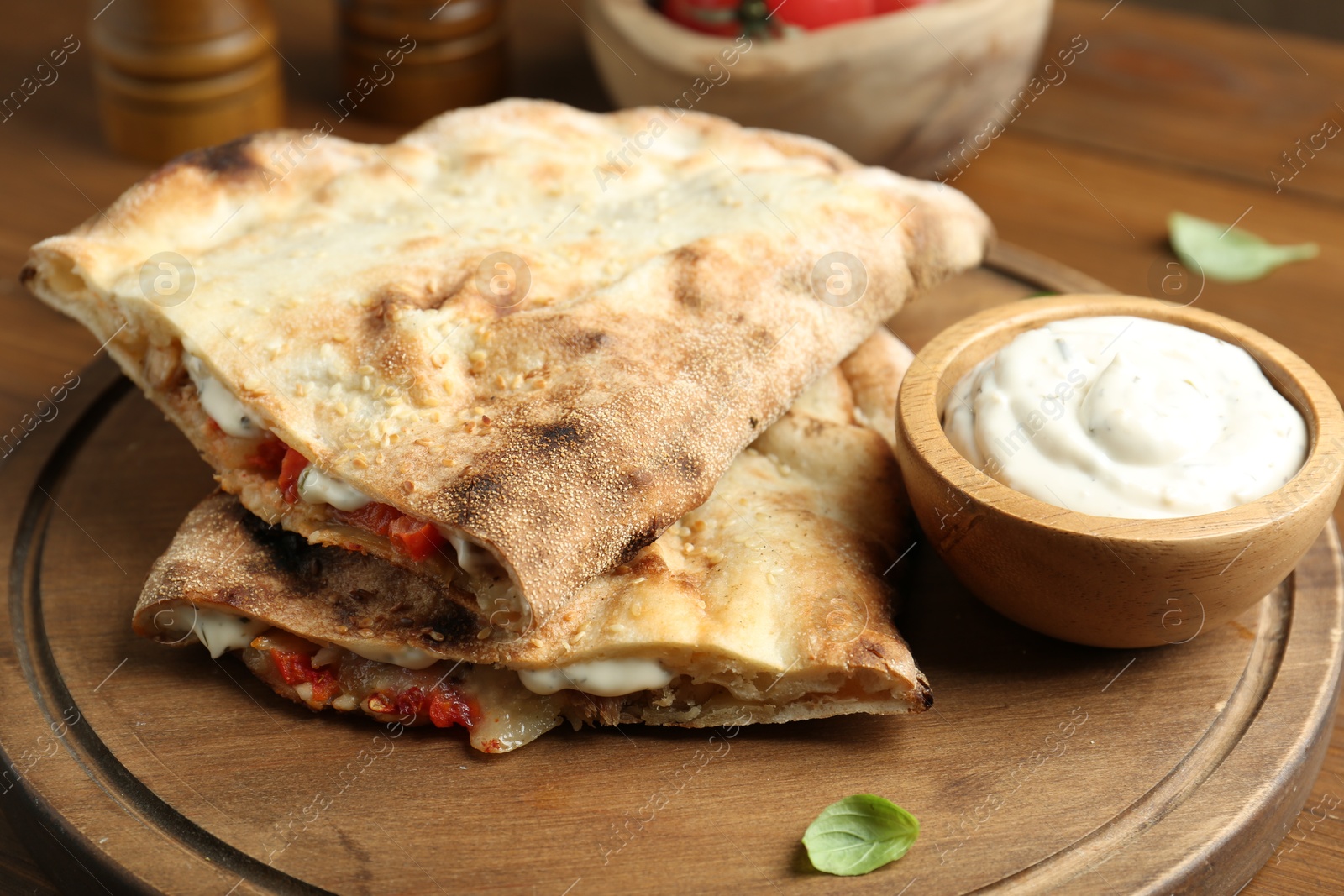 Photo of Halves of tasty calzone with meat, cheese, sauce and tomato on wooden table, closeup