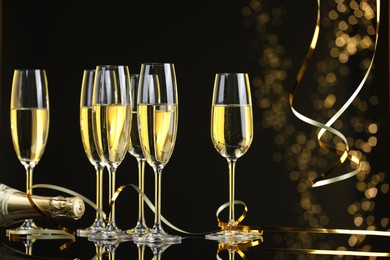 Photo of Champagne in glasses and bottle on mirror surface against black background with blurred lights