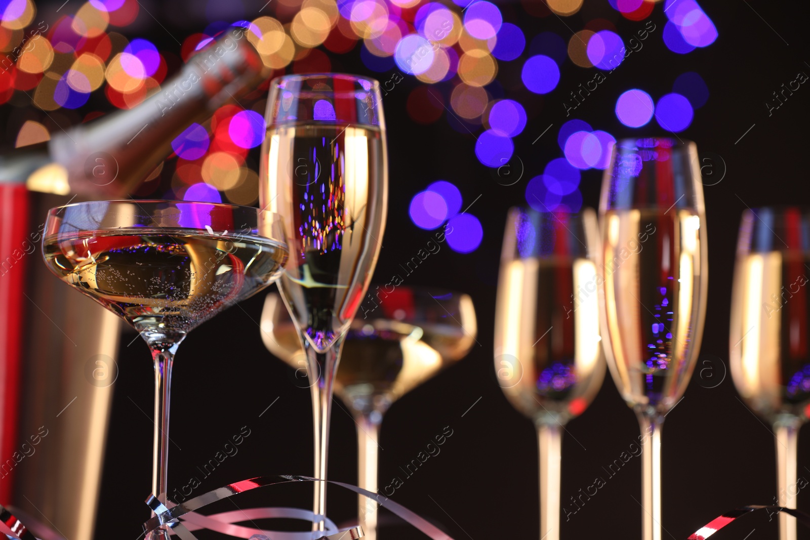 Photo of Champagne in glasses and party streamers against black background with blurred lights