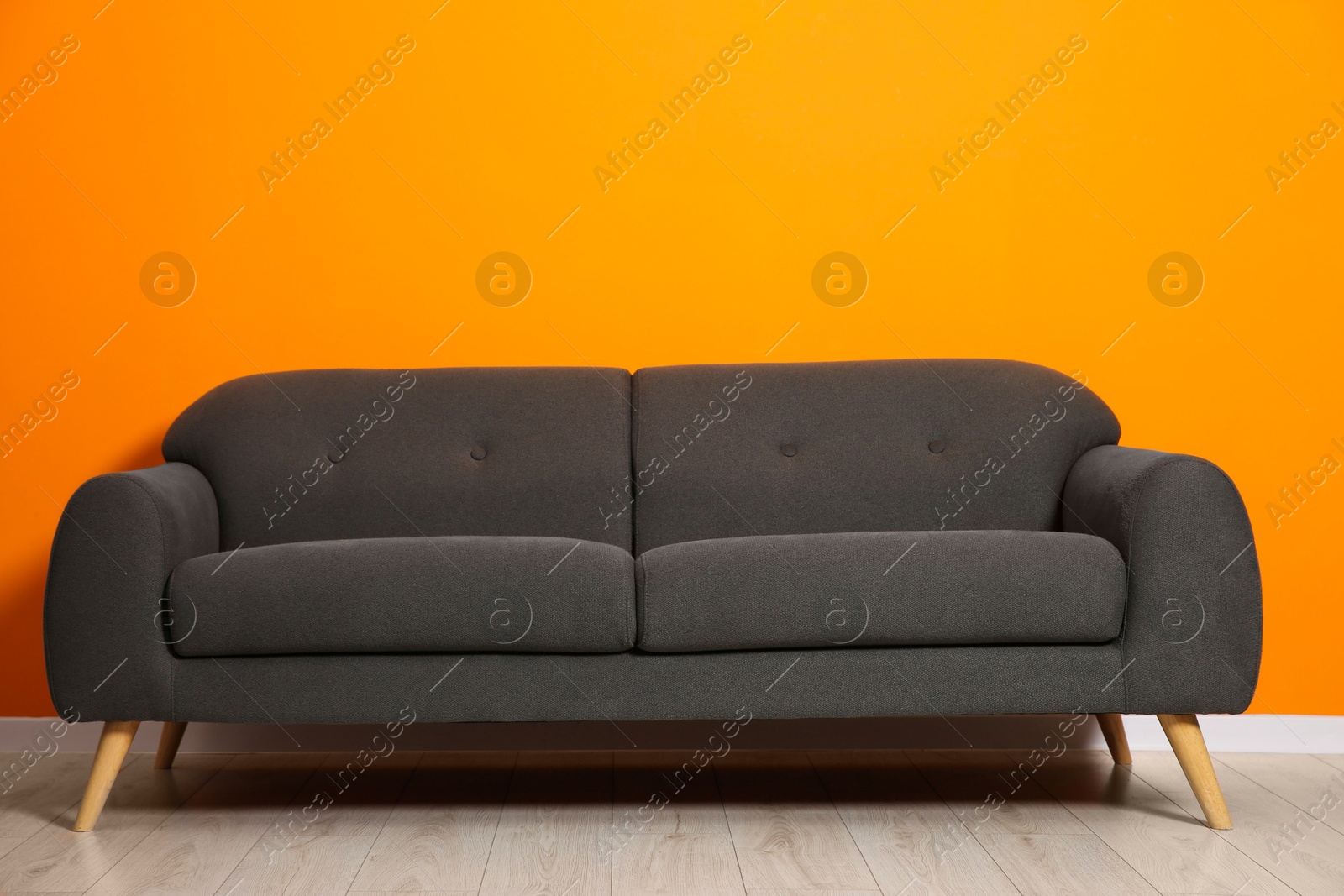 Photo of One stylish grey sofa near orange wall