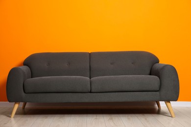 Photo of One stylish grey sofa near orange wall