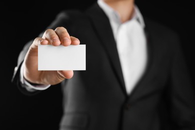 Photo of Man holding blank business card on black background, closeup. Mockup for design