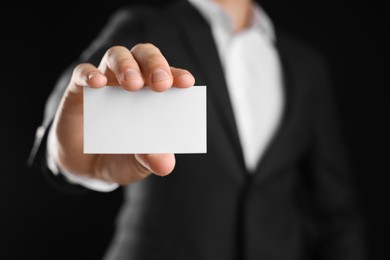 Photo of Man holding blank business card on black background, closeup. Mockup for design