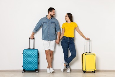 Happy woman and man with suitcases near light wall indoors