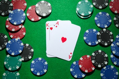 Photo of Poker chips and playing cards on green table, flat lay