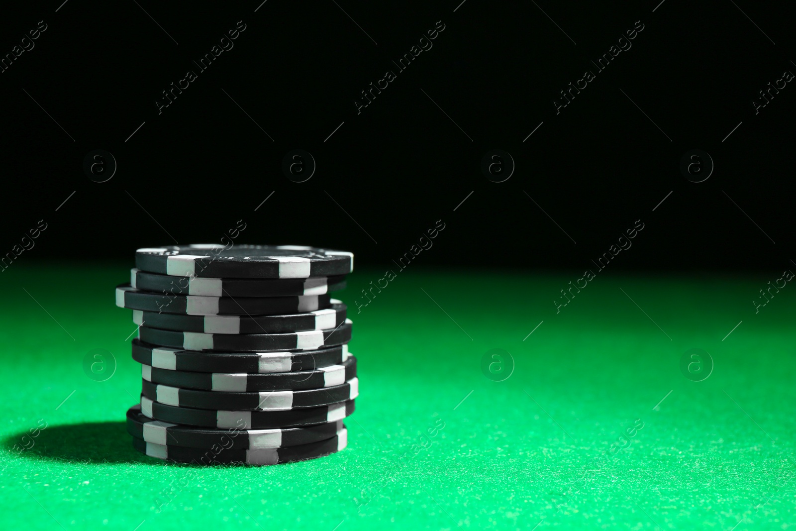 Photo of Stack of poker chips on green table against dark background, closeup. Space for text