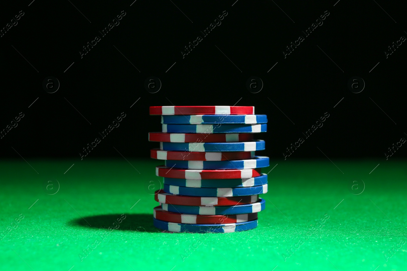 Photo of Stack of poker chips on green table against dark background, closeup