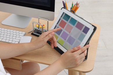 Photo of Designer working on tablet at wooden table indoors, closeup