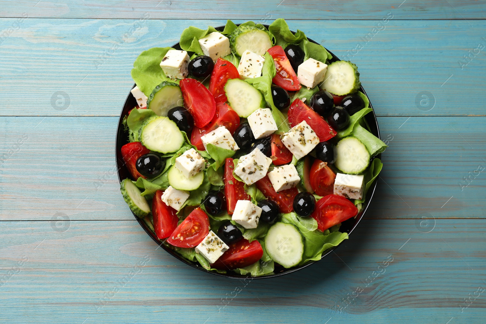 Photo of Delicious salad with feta cheese on light blue wooden table, top view