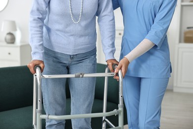 Photo of Nurse helping senior woman with walking frame indoors, closeup