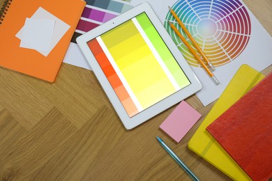 Photo of Designer's workplace with tablet, palettes and stationery on wooden table, flat lay