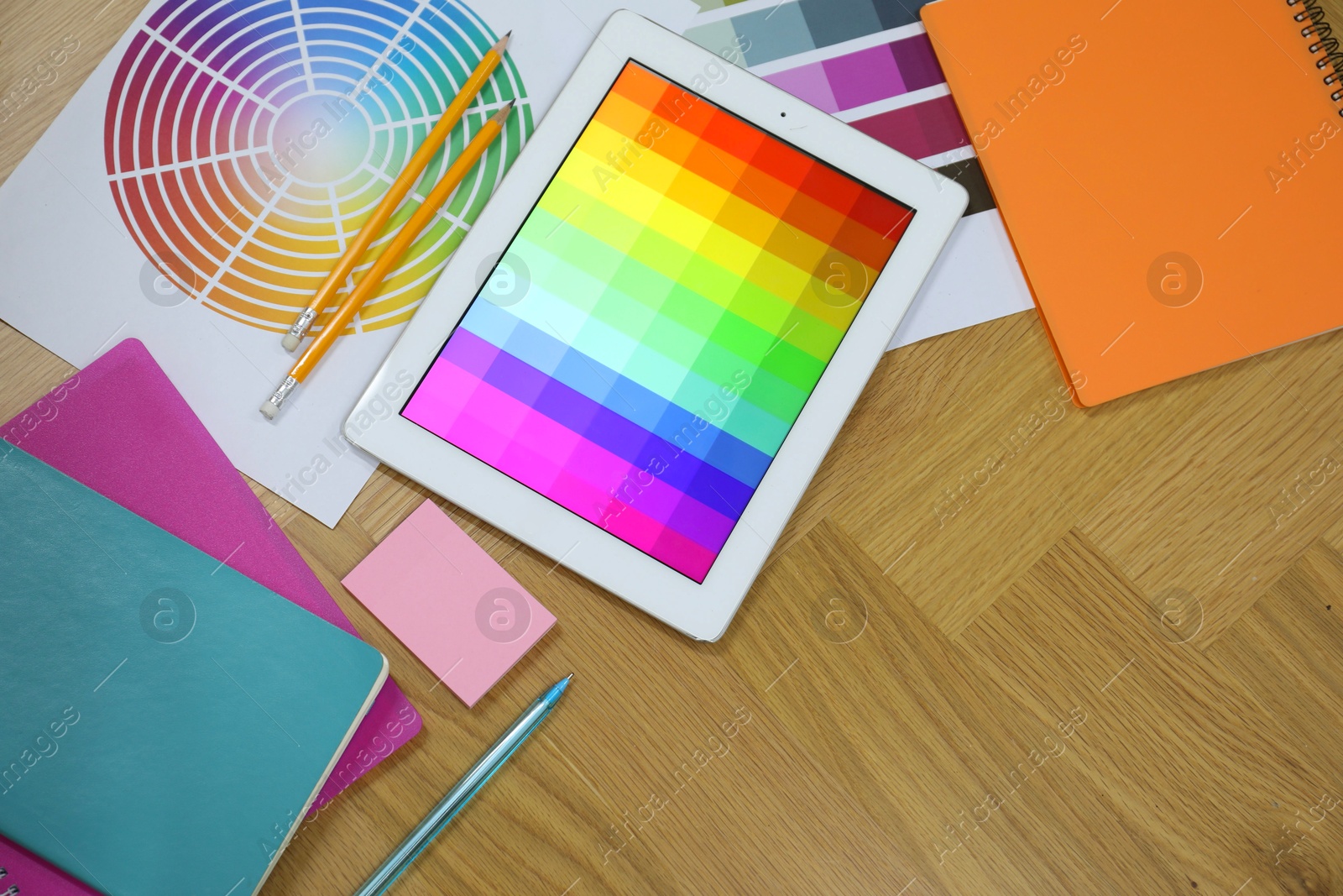 Photo of Designer's workplace with tablet, palettes and stationery on wooden table, flat lay