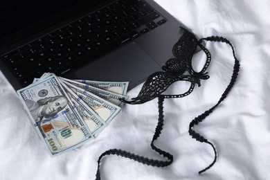 Photo of Prostitution and virtual sex. Laptop, dollar banknotes and mask on linens