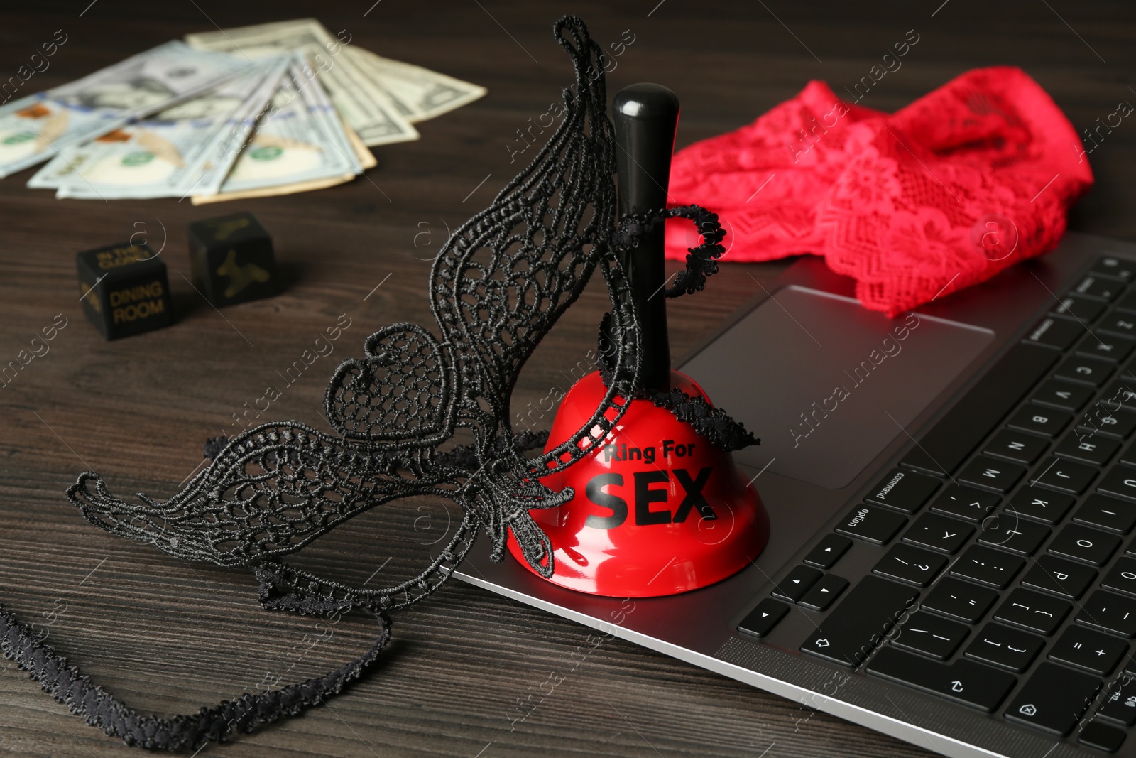 Photo of Sex work. Laptop, lingerie, bell, mask and money on wooden surface, closeup