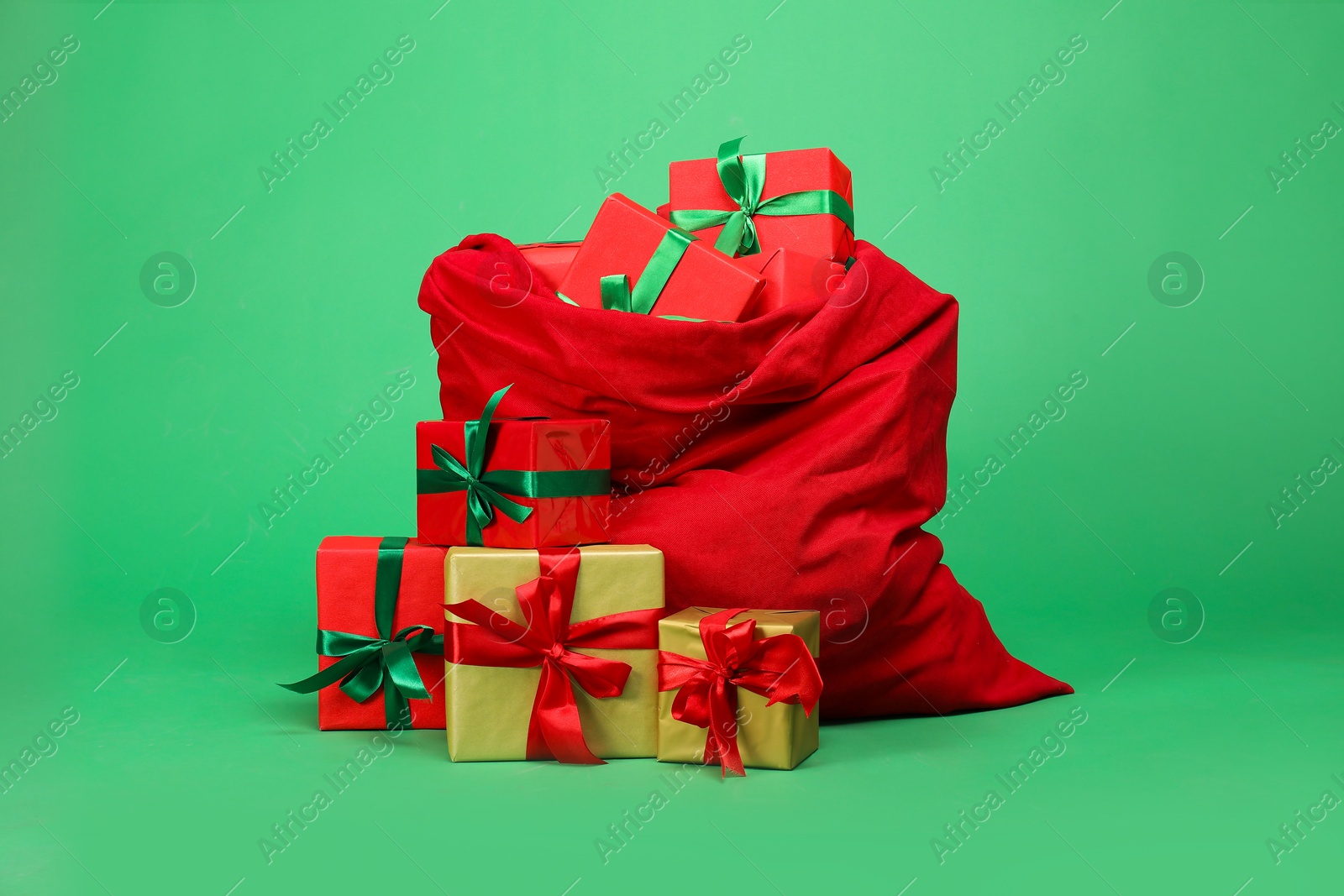 Photo of Red Santa Claus bag with gift boxes on green background