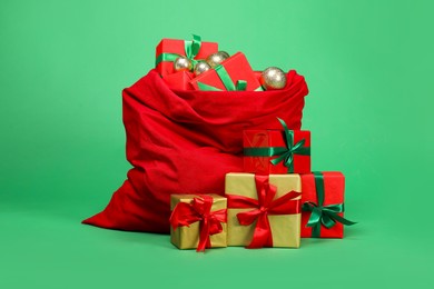 Photo of Red Santa Claus bag with baubles and gift boxes on green background