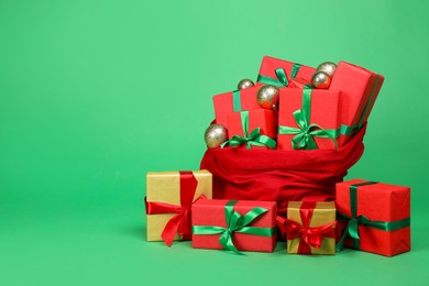 Photo of Red Santa Claus bag with baubles and gift boxes on green background, space for text