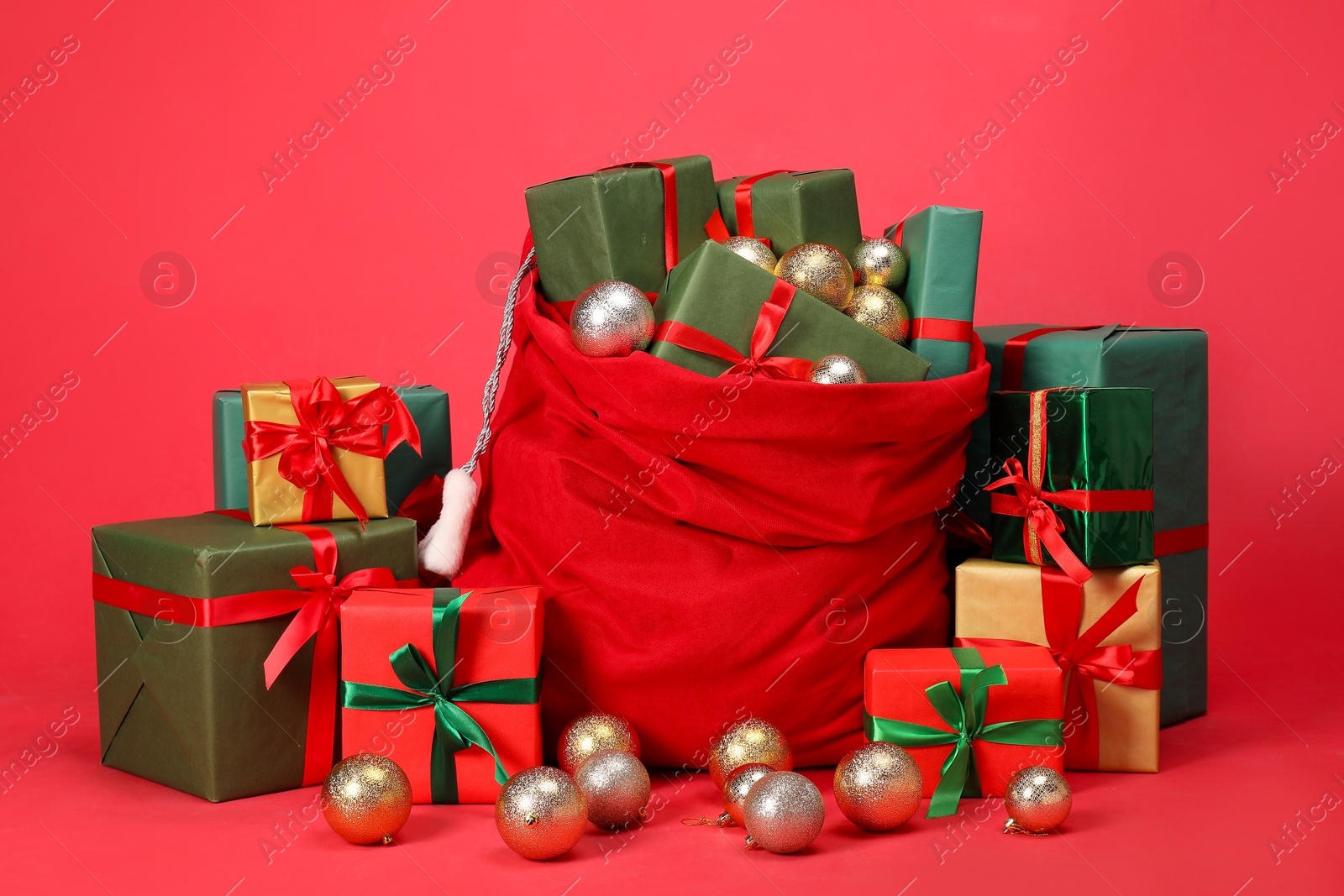 Photo of Santa Claus bag with baubles and gift boxes on red background